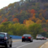 A bridge with cars heading toward a mountain covered in trees with fall foliage.
